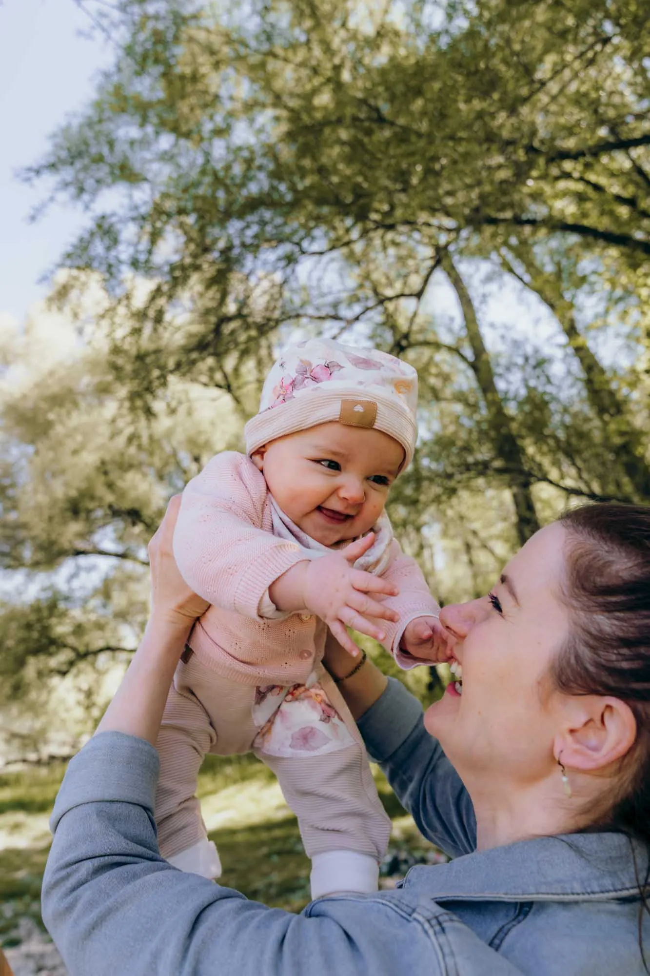 Mutter hebt ihr Baby beim Frühlingsshooting im Grünen hoch